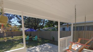 A covered patio with a swing chair, a table with chairs, and a blue umbrella. - Cute Bungalow in Historic Kenwood (St. Petersburg)