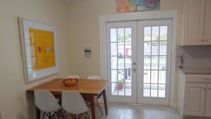 A dining area with a wooden table and white chairs, a painting on the wall, and a door leading outside. - Cute Bungalow in Historic Kenwood (St. Petersburg)