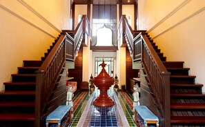 A grand staircase with a central decorative urn, flanked by statues, leading to a bright upper landing. - Samoeng Center (Samoeng)