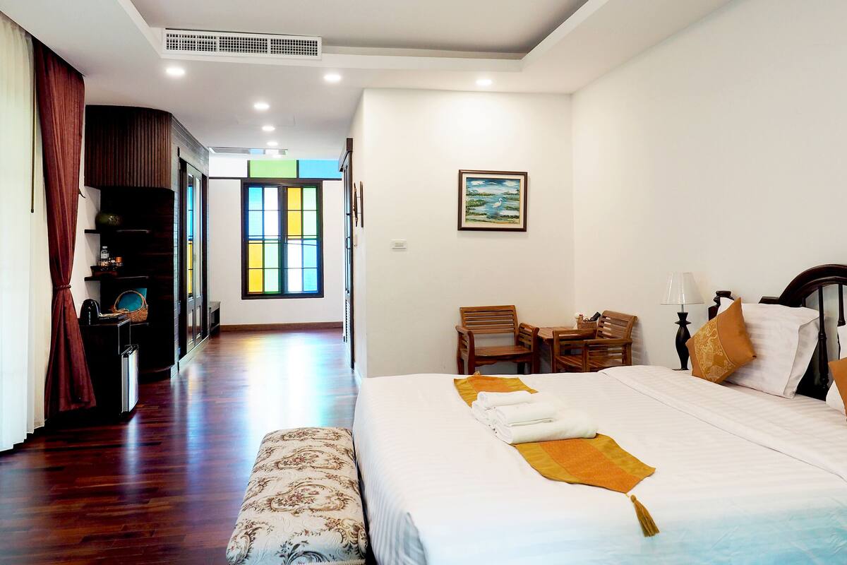 Una habitación de hotel con una cama grande, un banco de madera, un escritorio con una silla, una ventana con vistas y un cuadro en la pared.