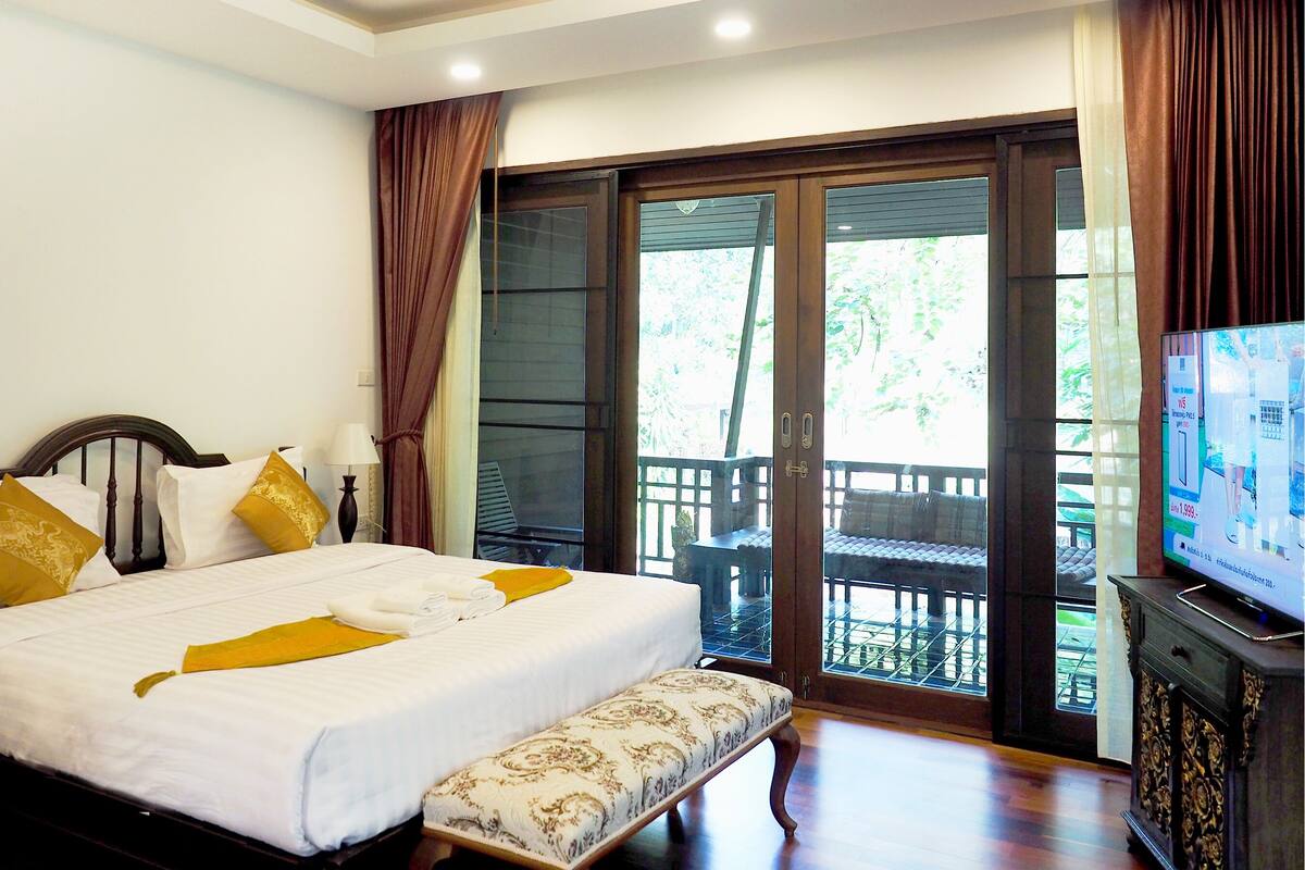Habitación de hotel con cama, un banco, televisor y puerta corrediza de vidrio al exterior.