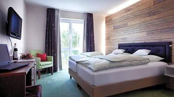 Ein Hotelzimmer mit Bett, Schreibtisch, Laptop, Fernseher und einem Fenster mit Vorhängen.