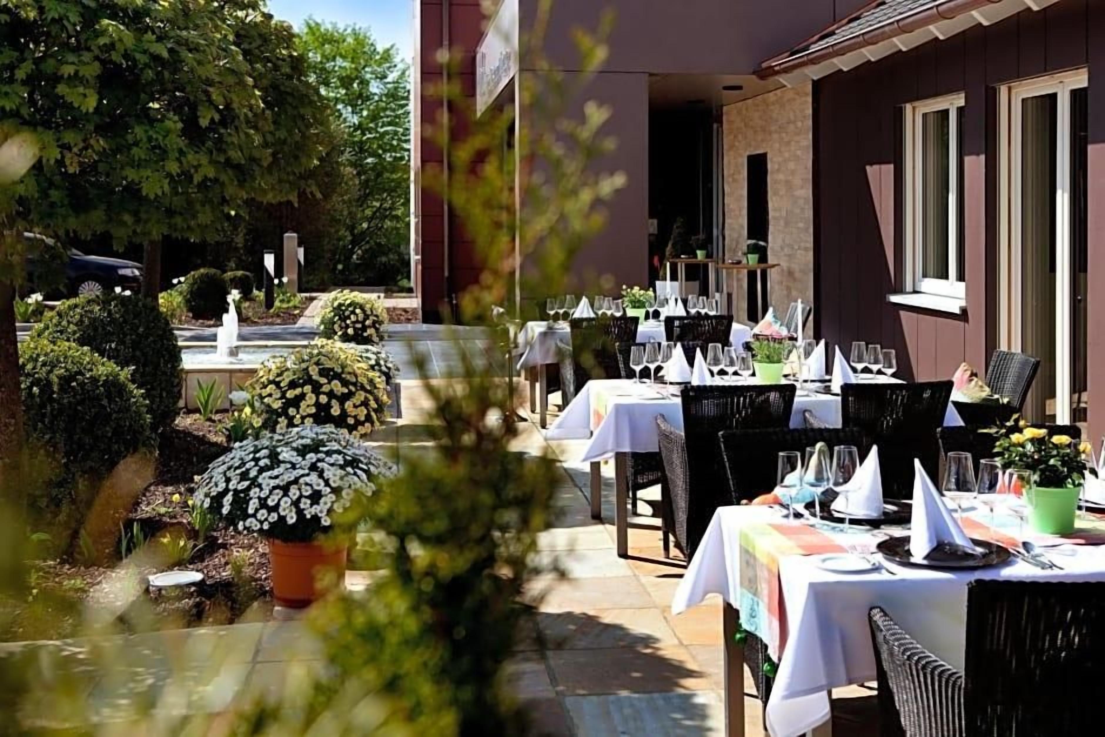 Un área de comedor al aire libre con mesas dispuestas para los huéspedes, rodeada de plantas en macetas y una fuente.