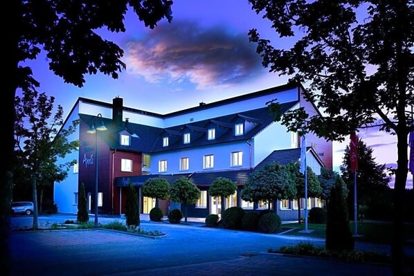 Un hotel de varios pisos con diseño moderno, que cuenta con un patio central con árboles y una entrada bien iluminada.