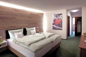 Une chambre à coucher avec une tête de lit en bois, un lit avec une literie verte, une table de chevet et une œuvre d’art accrochée au mur.