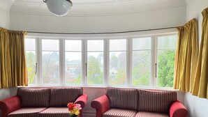 Una habitación con dos sofás rojos, una mesita con un jarrón de flores y ventanas amplias con cortinas.