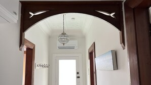 Un pasillo con una puerta blanca, un pequeño banco de madera y una lámpara en el techo.