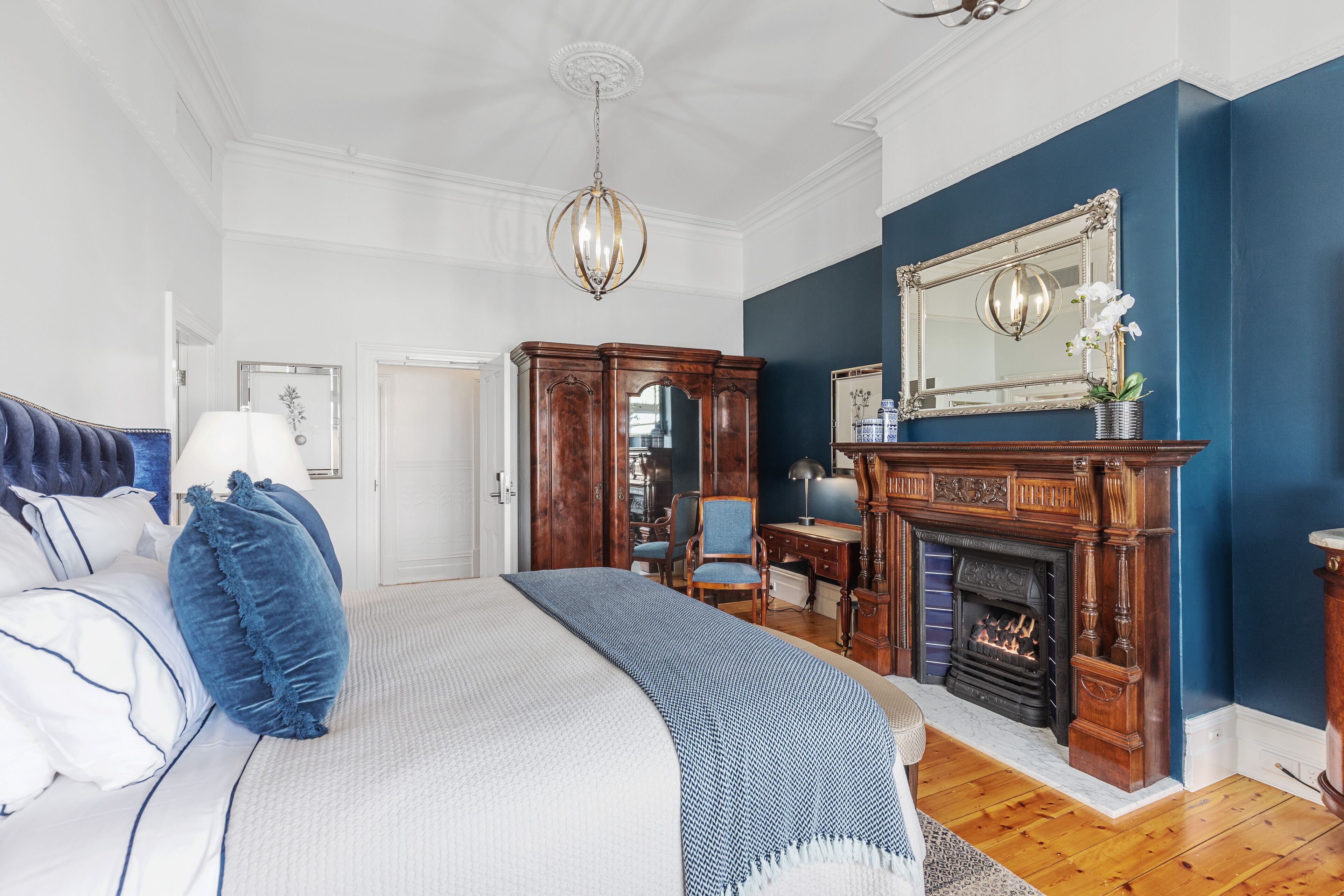 A bedroom with a large bed, a fireplace, a mirror, and a blue accent wall.