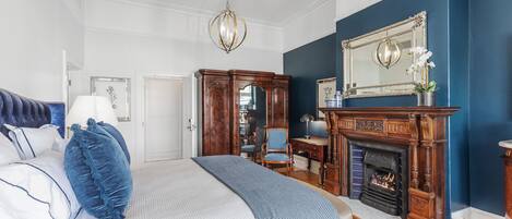 A bedroom with a large bed, a fireplace, a mirror, and a blue accent wall.