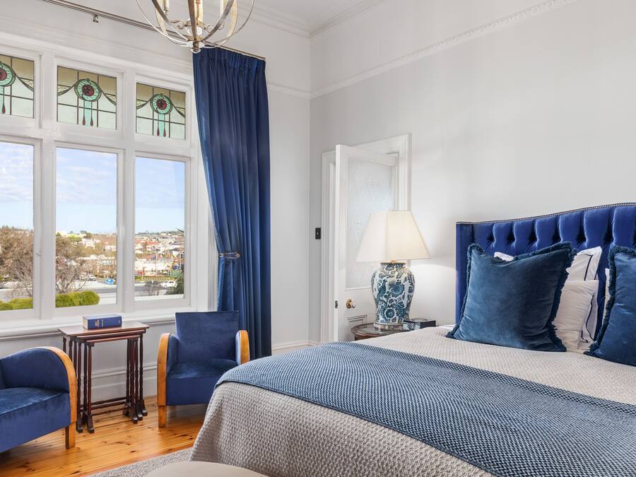 Un dormitorio con una cama grande, una mesita de noche, una lámpara, una silla y vistas al exterior.
