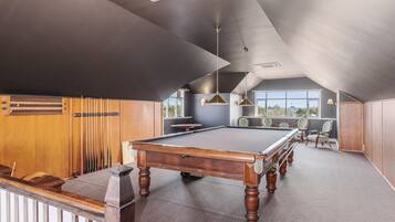 A pool table in a room with a sloped ceiling, wooden paneling, and large windows.
