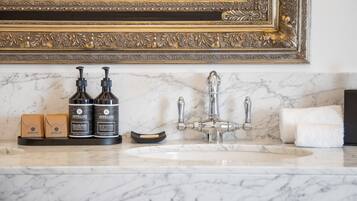 Um lavatório de banheiro com bancada de mármore, um espelho com moldura dourada e duas embalagens de Apelles body wash.