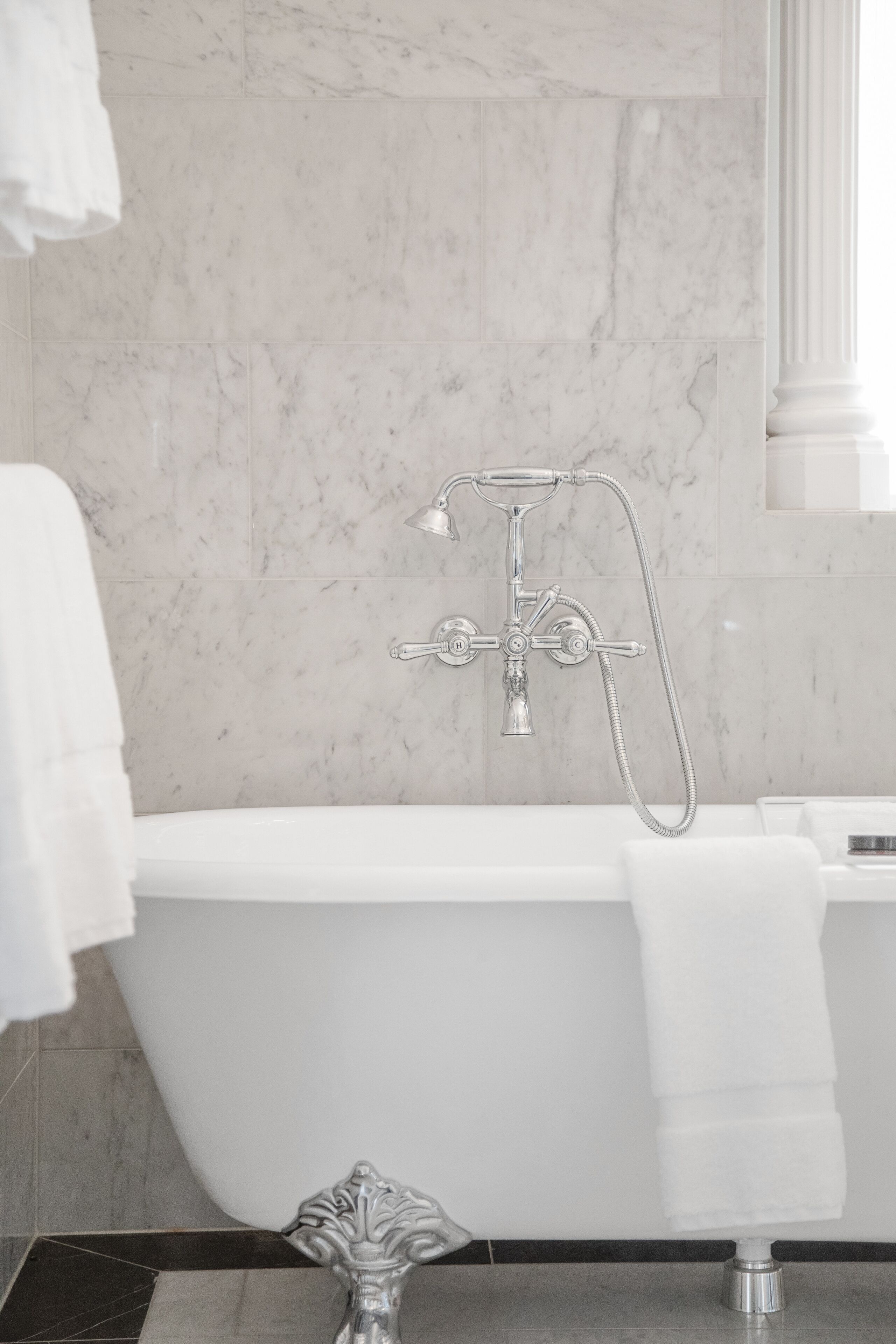 A modern bathroom with a freestanding bathtub, a showerhead, and a marble wall.