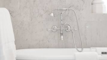 A modern bathroom with a freestanding bathtub, a showerhead, and a marble wall.