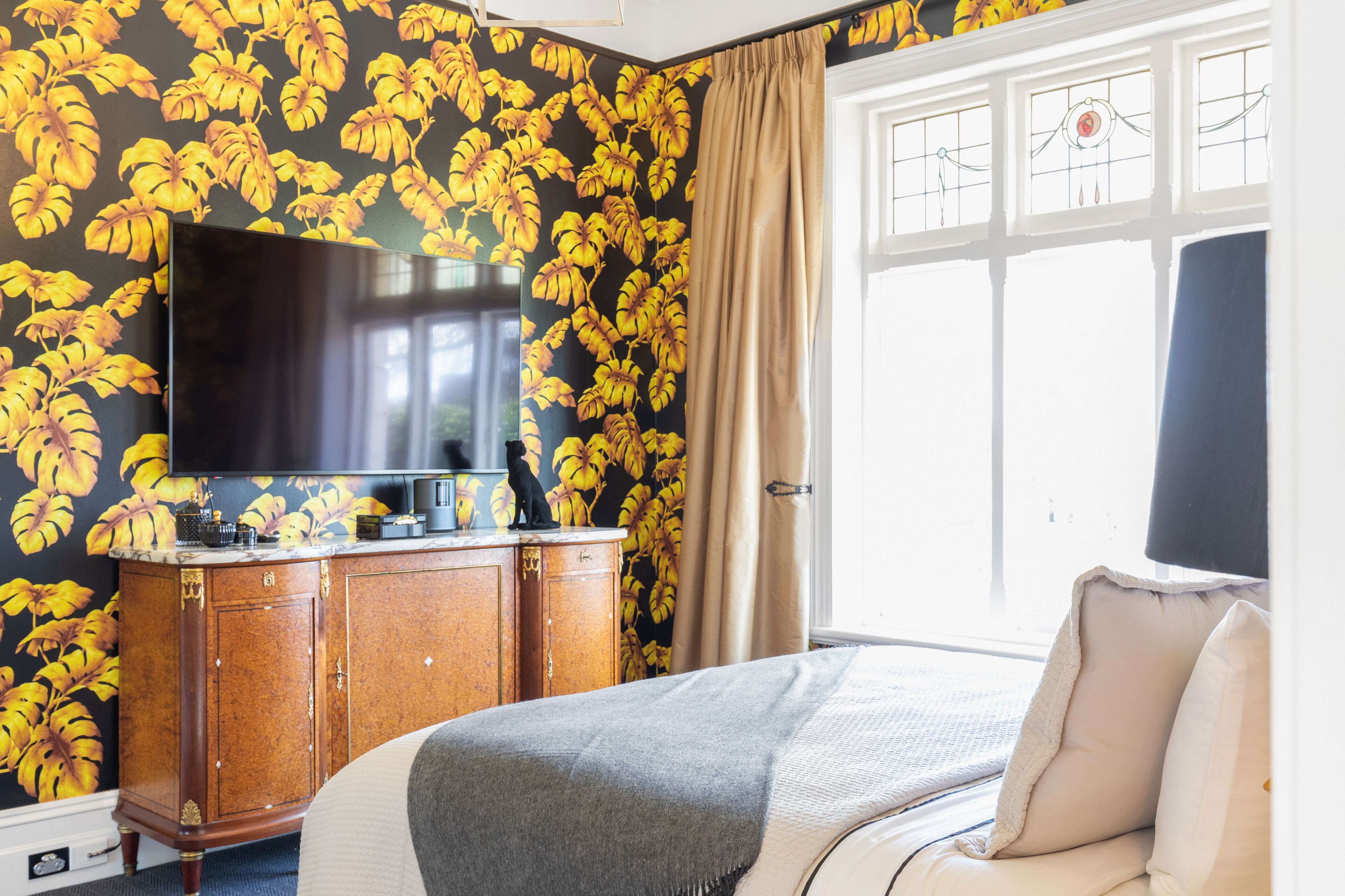 Habitación de hotel con una televisión de pantalla grande montada en la pared, un mueble de madera y una cama con manta gris.
