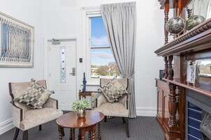 Una habitación con dos sillones, una mesita redonda con un florero, una chimenea y una puerta con ventanal.