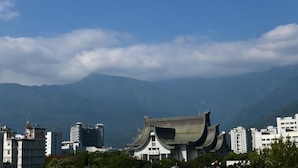 A traditional building with a curved roof, surrounded by modern high-rise buildings and mountains in the background. - Light Time B&B (Hualien City)
