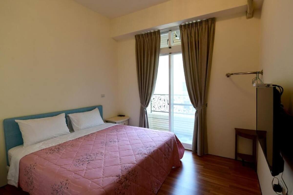 A bedroom with a bed, a nightstand, a TV, and a balcony with curtains.