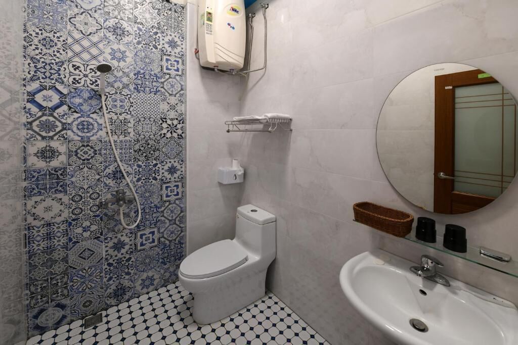 A bathroom with a white toilet, a shower with a white hose, a sink with a mirror, and patterned tiles on the walls.