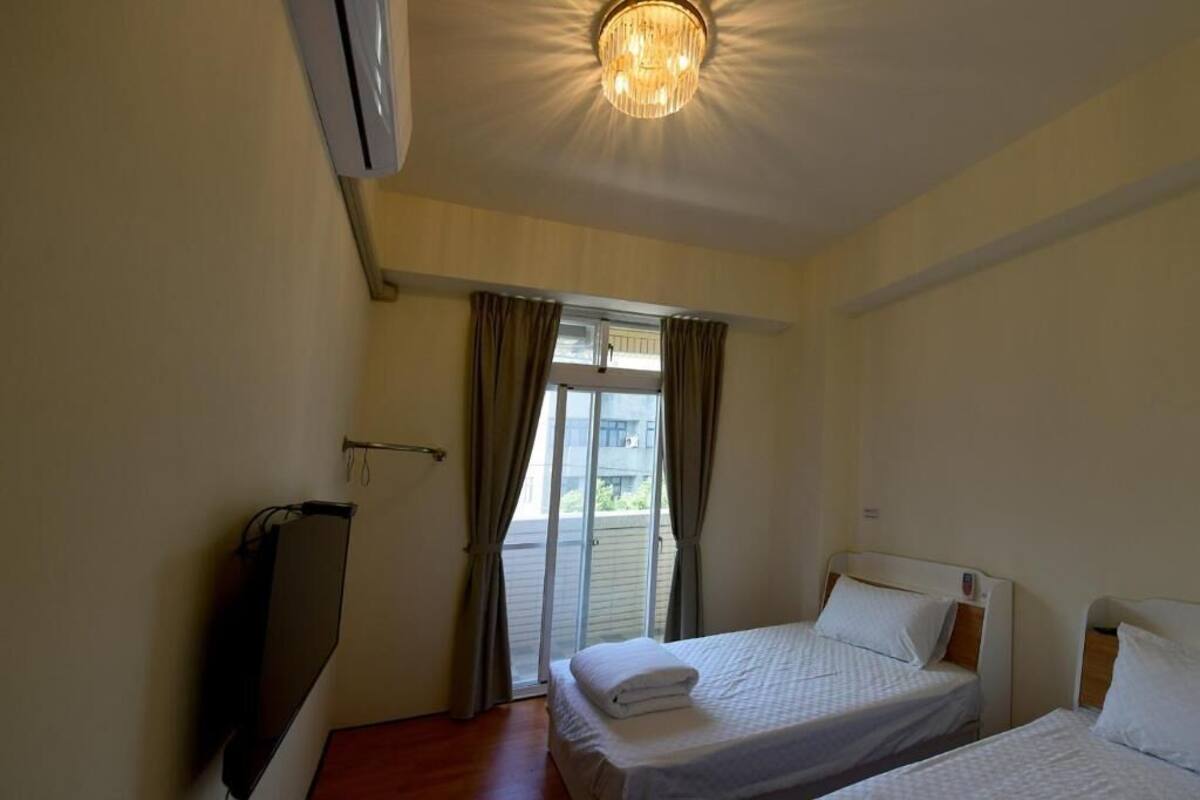 A hotel room with two beds, a ceiling light, and a sliding glass door leading to an outdoor area.