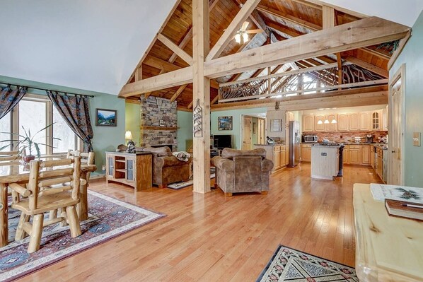 A spacious living area with a high wooden ceiling, a stone fireplace, and a kitchen with wooden cabinets. - 🌲 Our Cabin Is Ready When You’re Ready🌲 (Delavan)