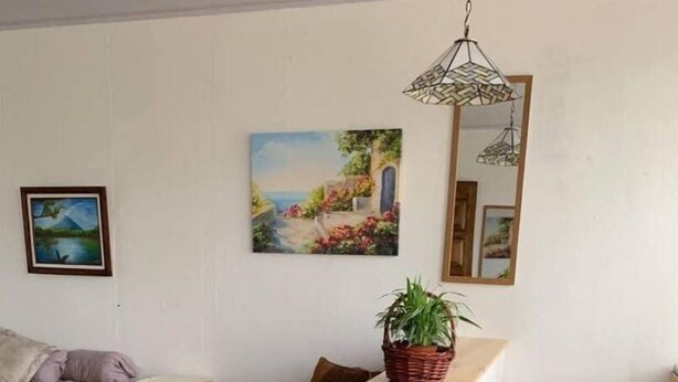 A small, cozy room with a bed, a wooden stool, a small table, and a chair. There is a painting on the wall and a hanging light fixture. - Costa Rica: Studio Close to EVERYTHING (Heredia)