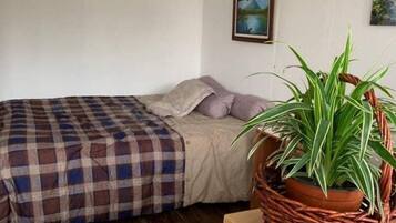 Un dormitorio con una cama, una mesita de noche de madera, una planta en maceta y un cuadro en la pared.