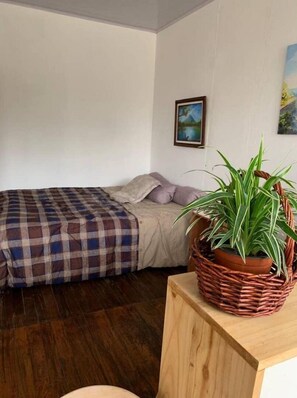 Ein Schlafzimmer mit einem Bett, einem Nachttisch aus Holz, einer Topfpflanze und einem Bild an der Wand.