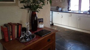 Een keuken met witte kastjes, een stenen vloer, een vaas met groene bladeren, een dienblad met wijnglazen, en een boek getiteld 'Indii of Clare'.