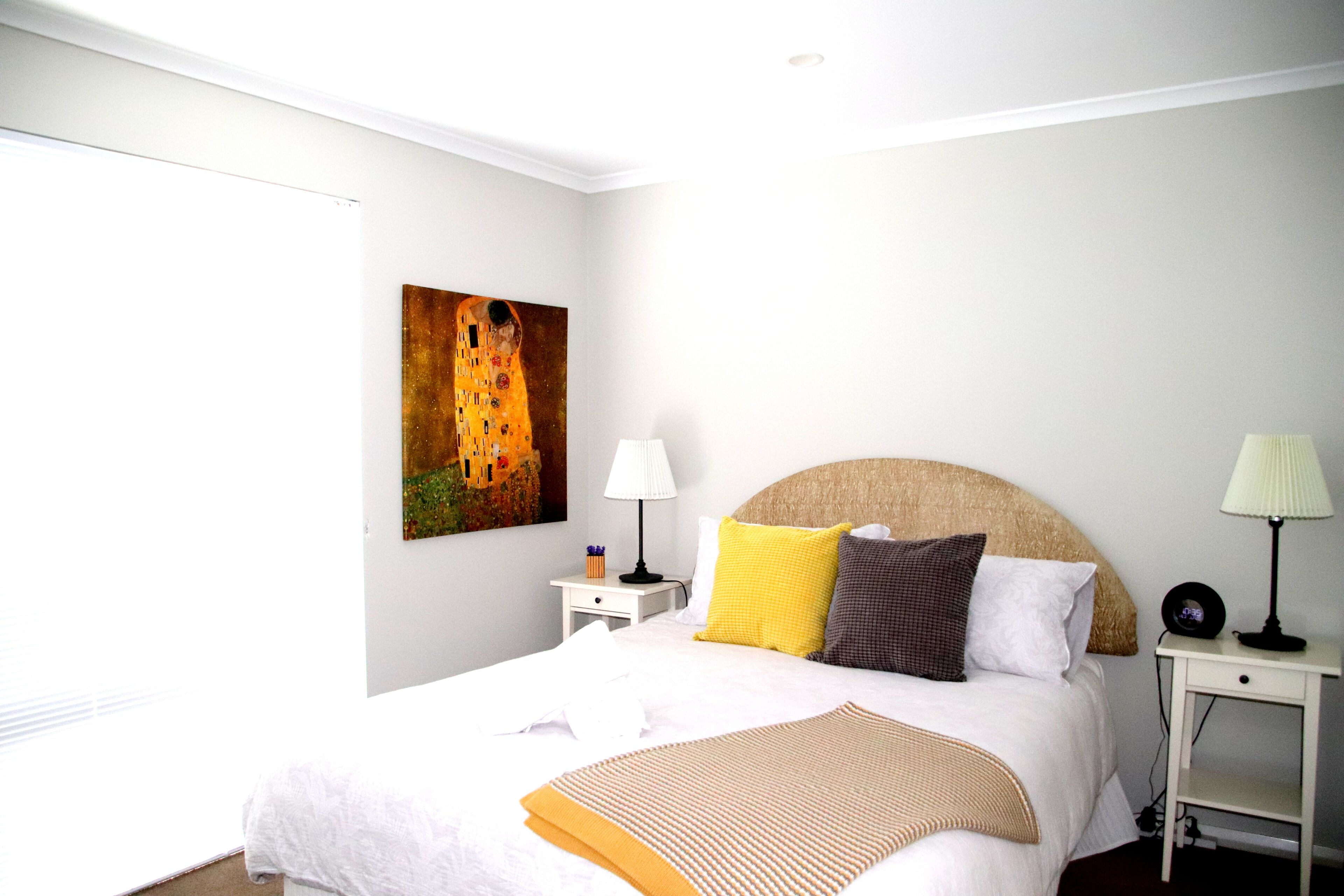 Habitación de hotel ordenada con una cama grande, cabecero, dos mesitas de noche, una lámpara y un cuadro en la pared.