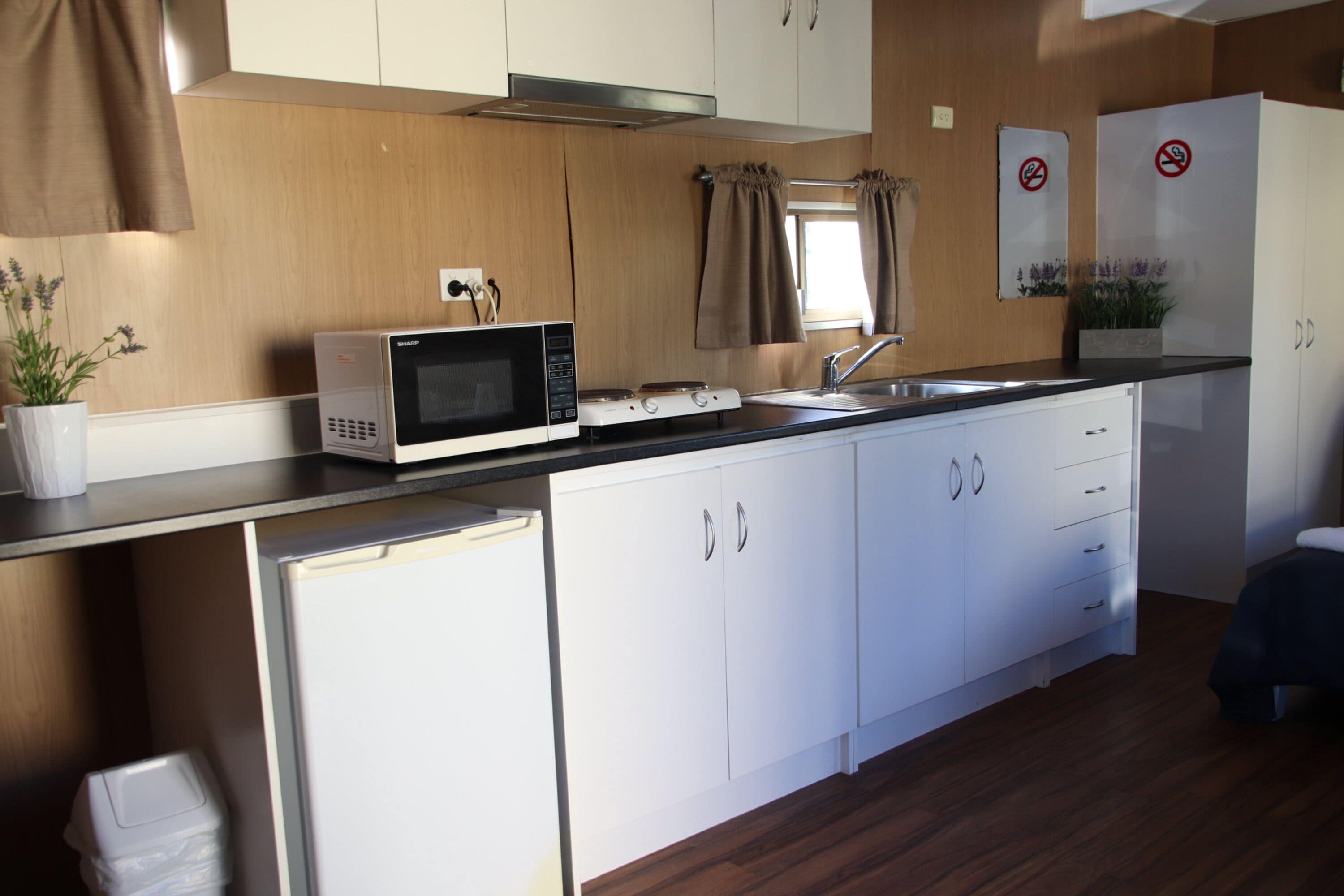 Una cocina compacta con armarios blancos, un microondas, un refrigerador pequeño y un lavamanos.