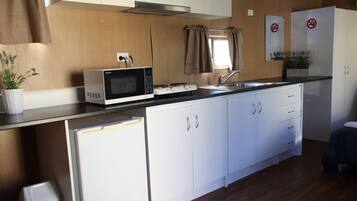 Una cocina compacta con armarios blancos, un microondas, un refrigerador pequeño y un lavamanos.