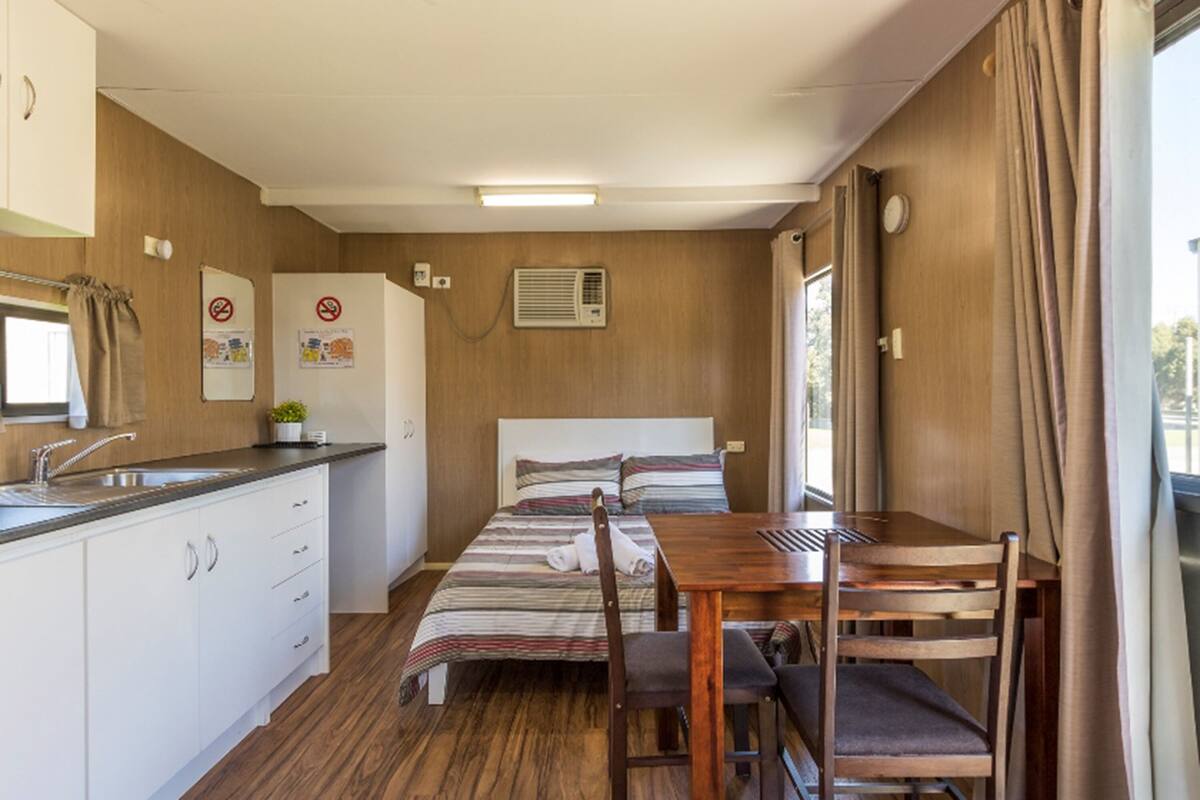 A compact room with a bed, a small kitchenette, a dining table, and a window with curtains.