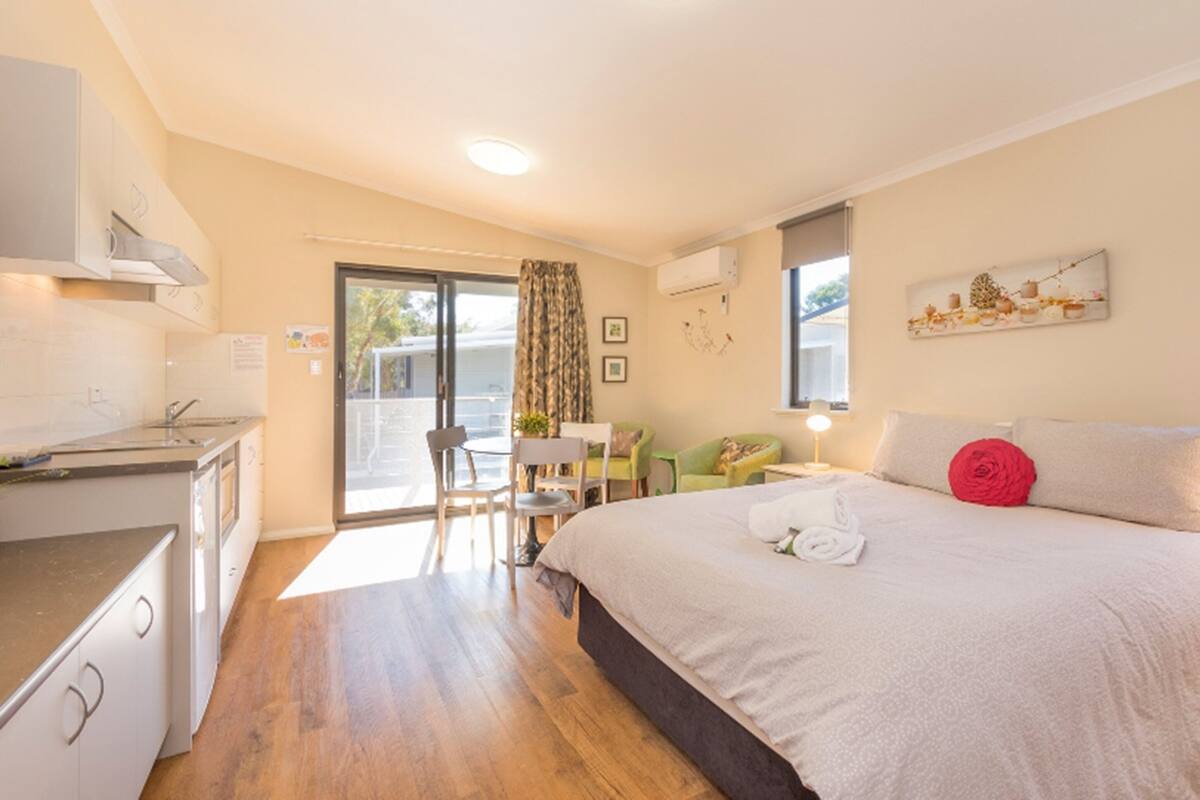 A bedroom with a bed, a desk, a chair, and a kitchenette.