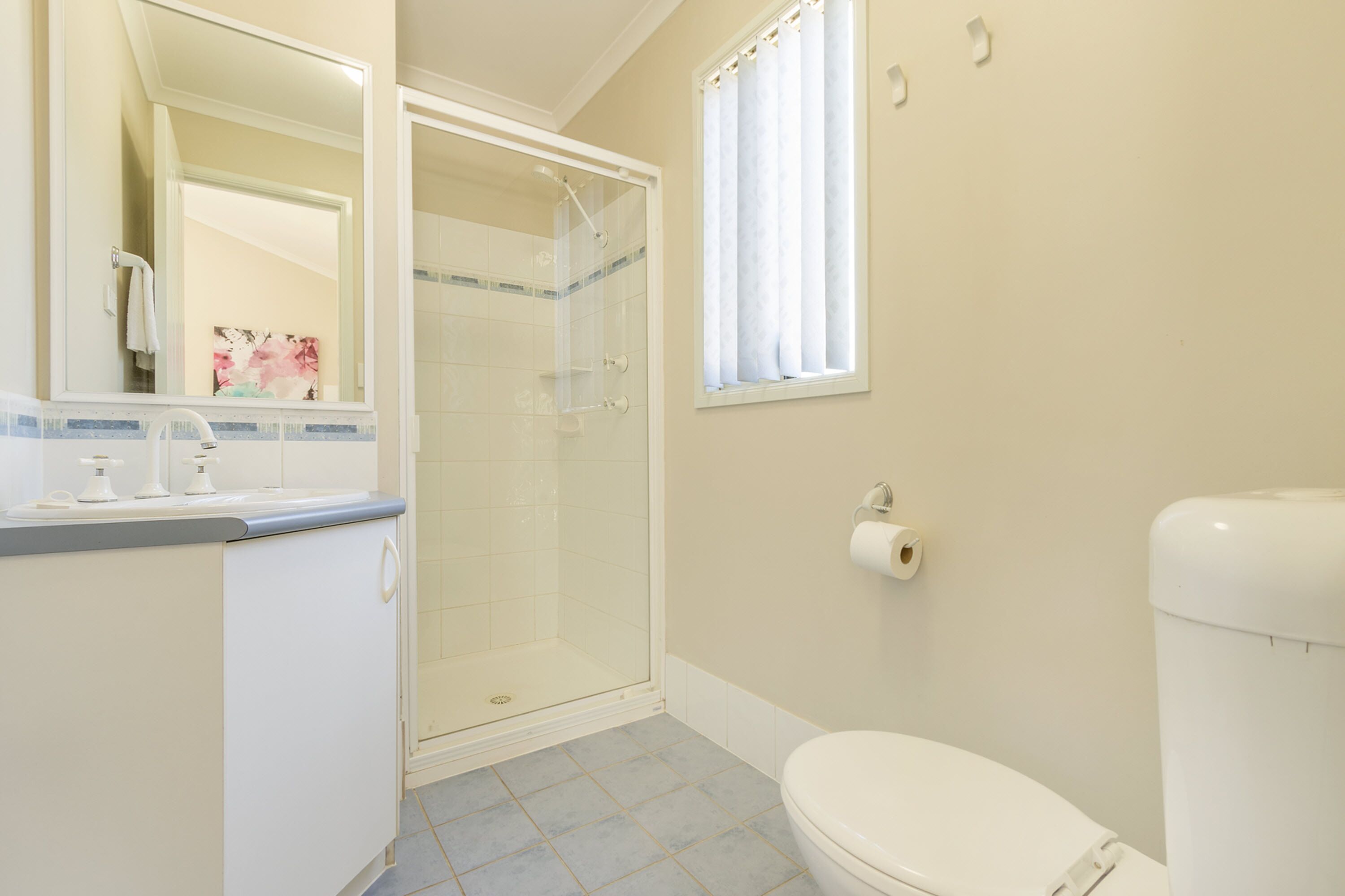 A bathroom with a toilet, a sink, a shower, and a window with curtains.