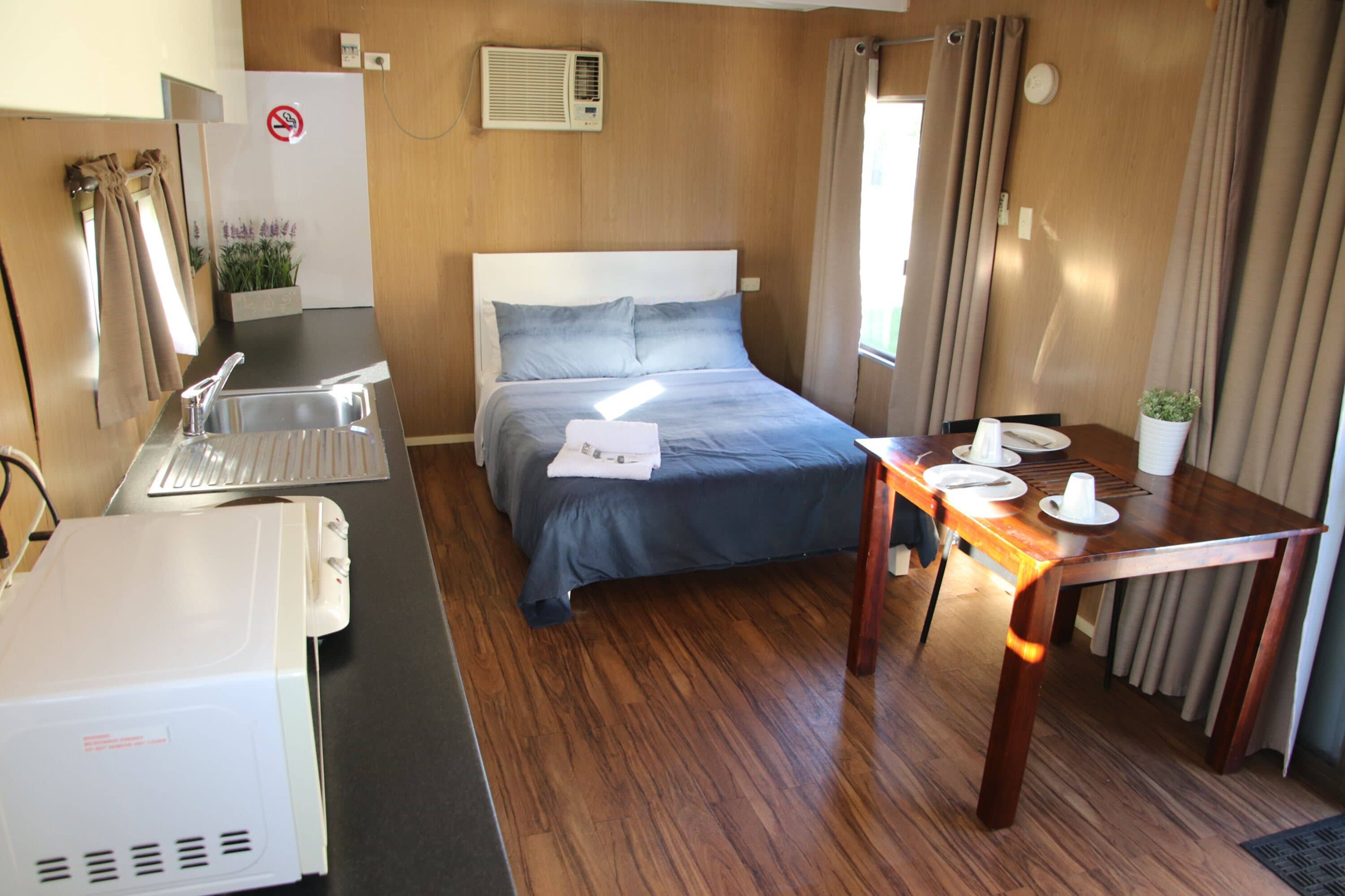 A hotel room with a bed, a desk with a sink, a table set for dining, and a small plant.