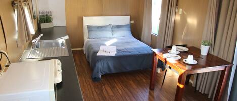 A hotel room with a bed, a desk with a sink, a table set for dining, and a small plant.