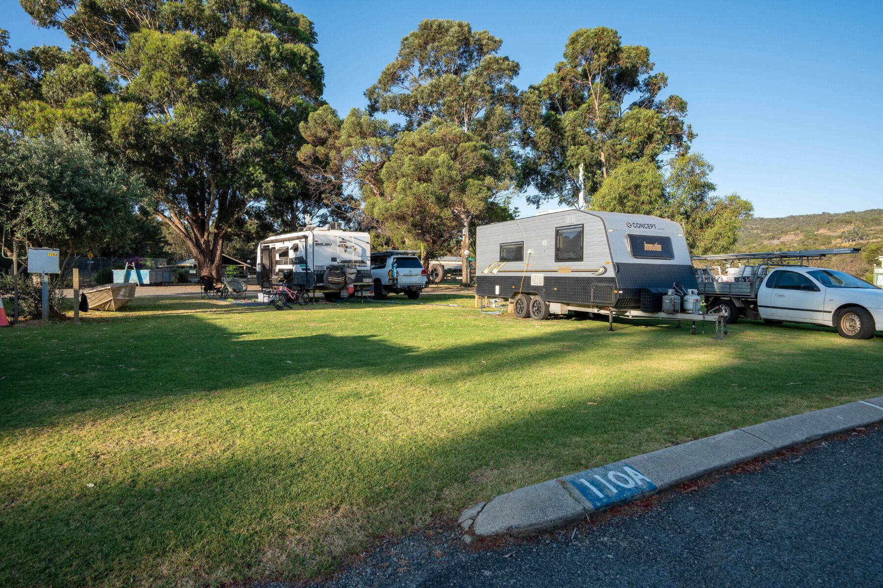 Um camping com veículos recreativos, uma área pavimentada e uma placa indicando vaga de estacionamento.