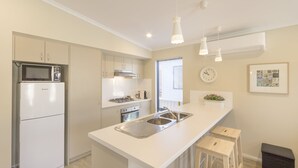Una cocina moderna con armarios blancos, microondas integrado, pileta de acero inoxidable e iluminación colgante.
