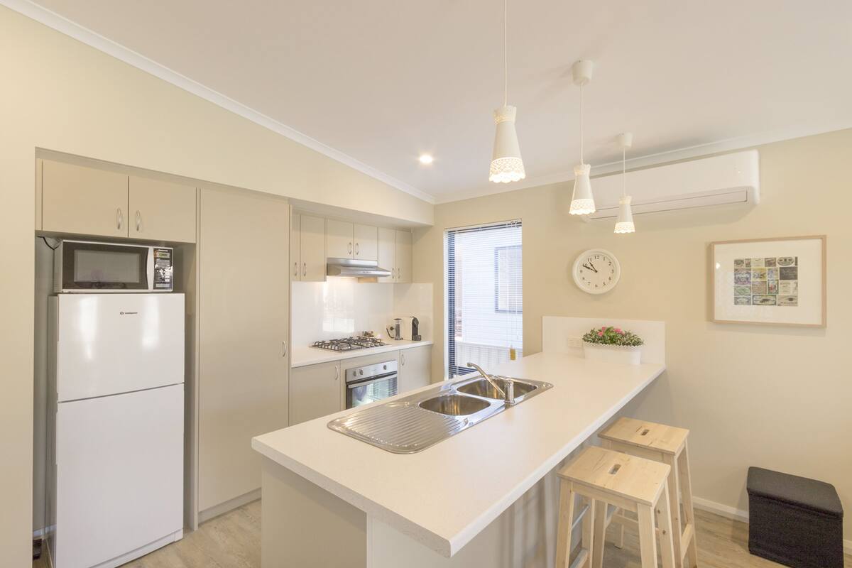 A modern kitchen with white cabinetry, a built-in microwave, a stainless steel sink, and pendant lighting.
