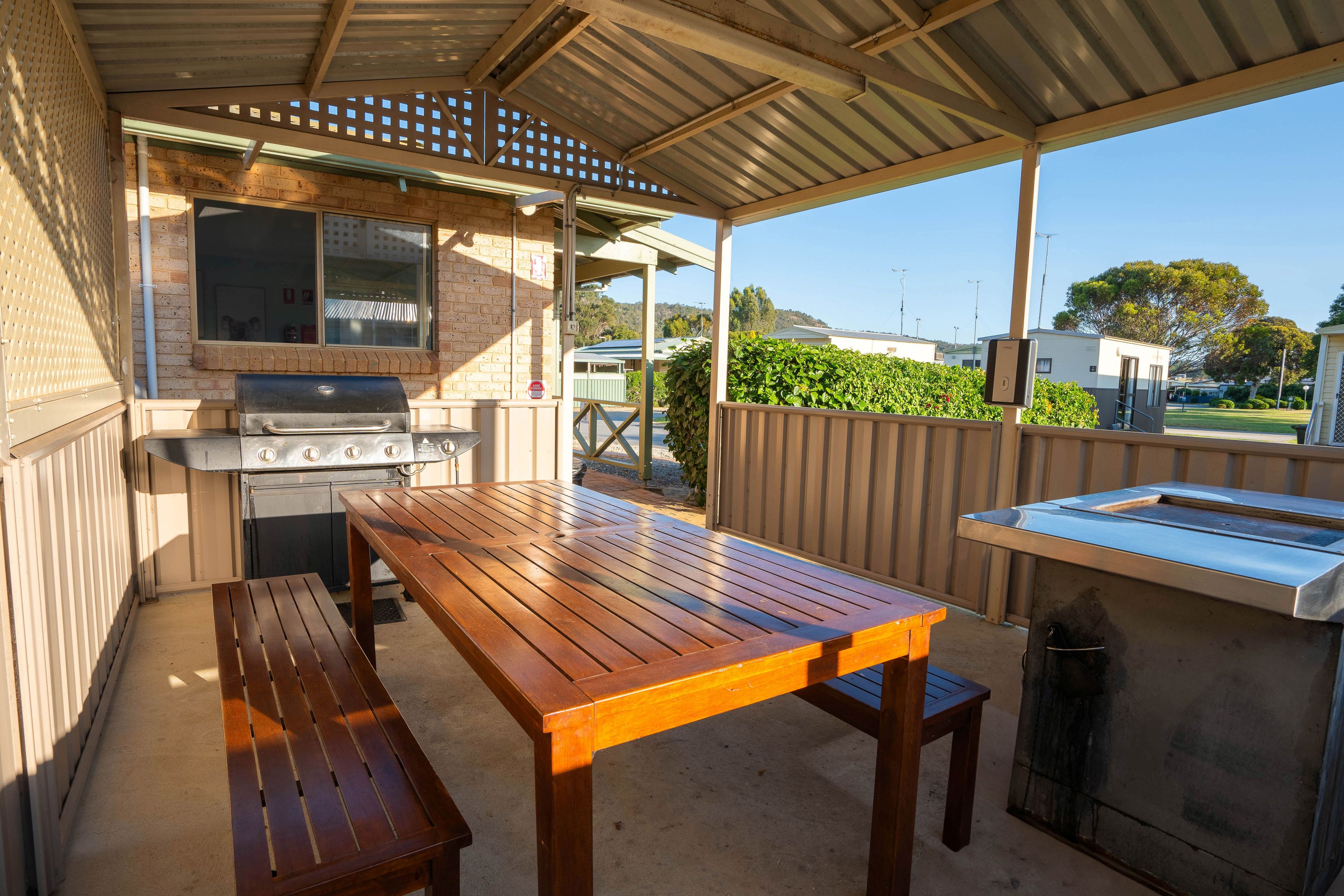 An outdoor patio with a barbecue grill, wooden table, and benches.