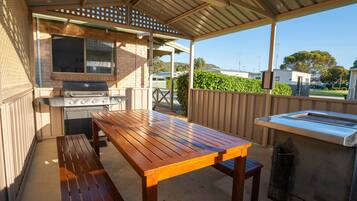 An outdoor patio with a barbecue grill, wooden table, and benches.