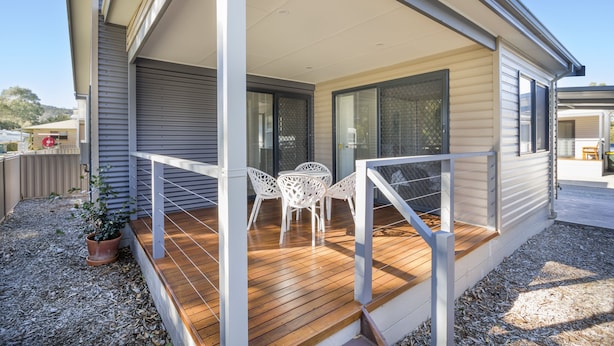 Una casa moderna con terraza de madera, mobiliario exterior blanco y un porche cubierto.