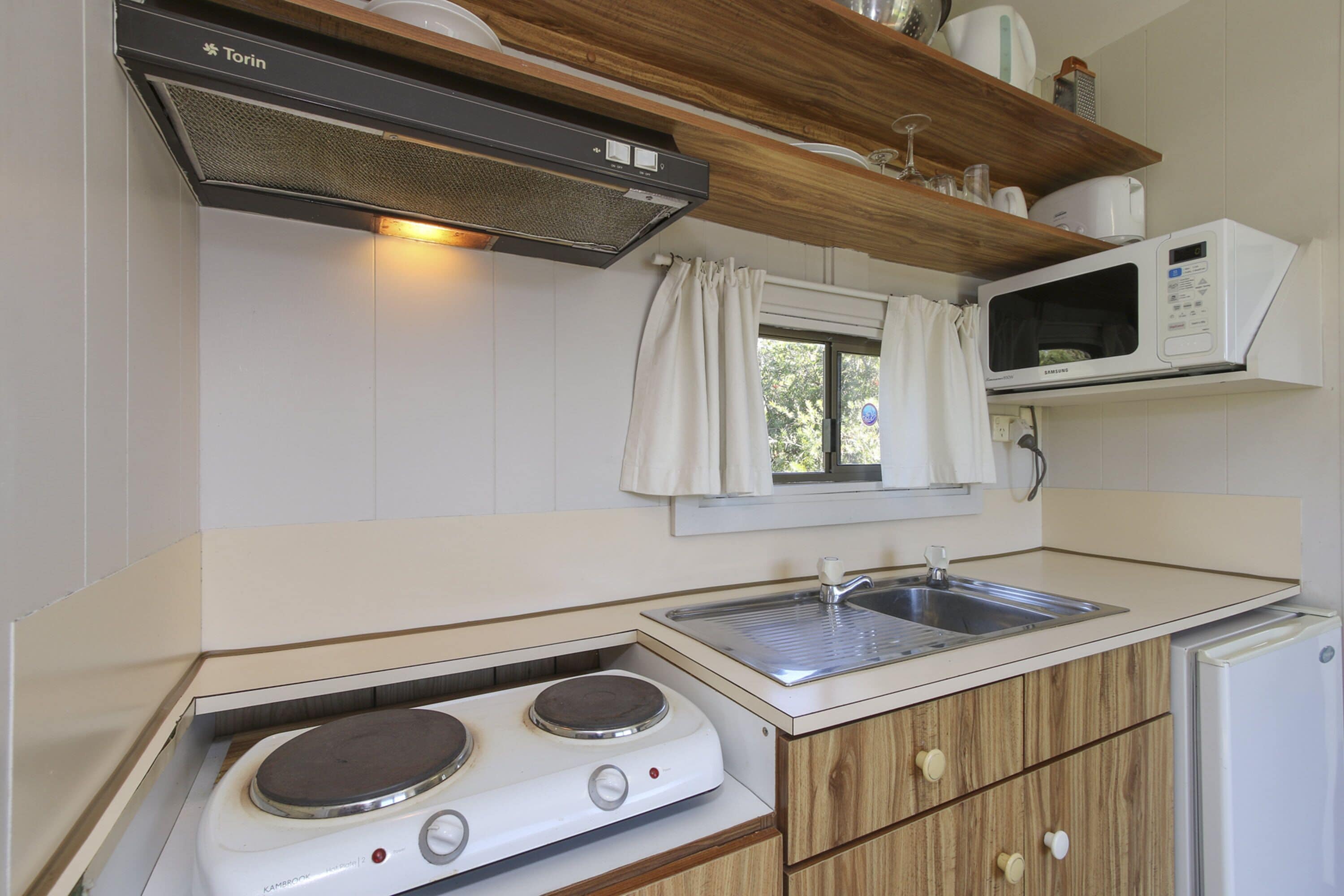 A compact kitchen with a stove, sink, microwave, and a small refrigerator.