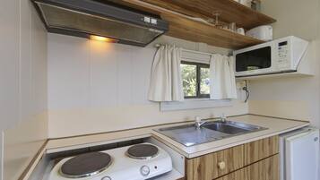 A compact kitchen with a stove, sink, microwave, and a small refrigerator.