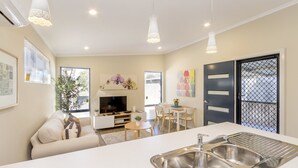 Una cocina moderna con lavaplatos integrado, un comedor con mesa y sillas, un sofá y un televisor en la sala.