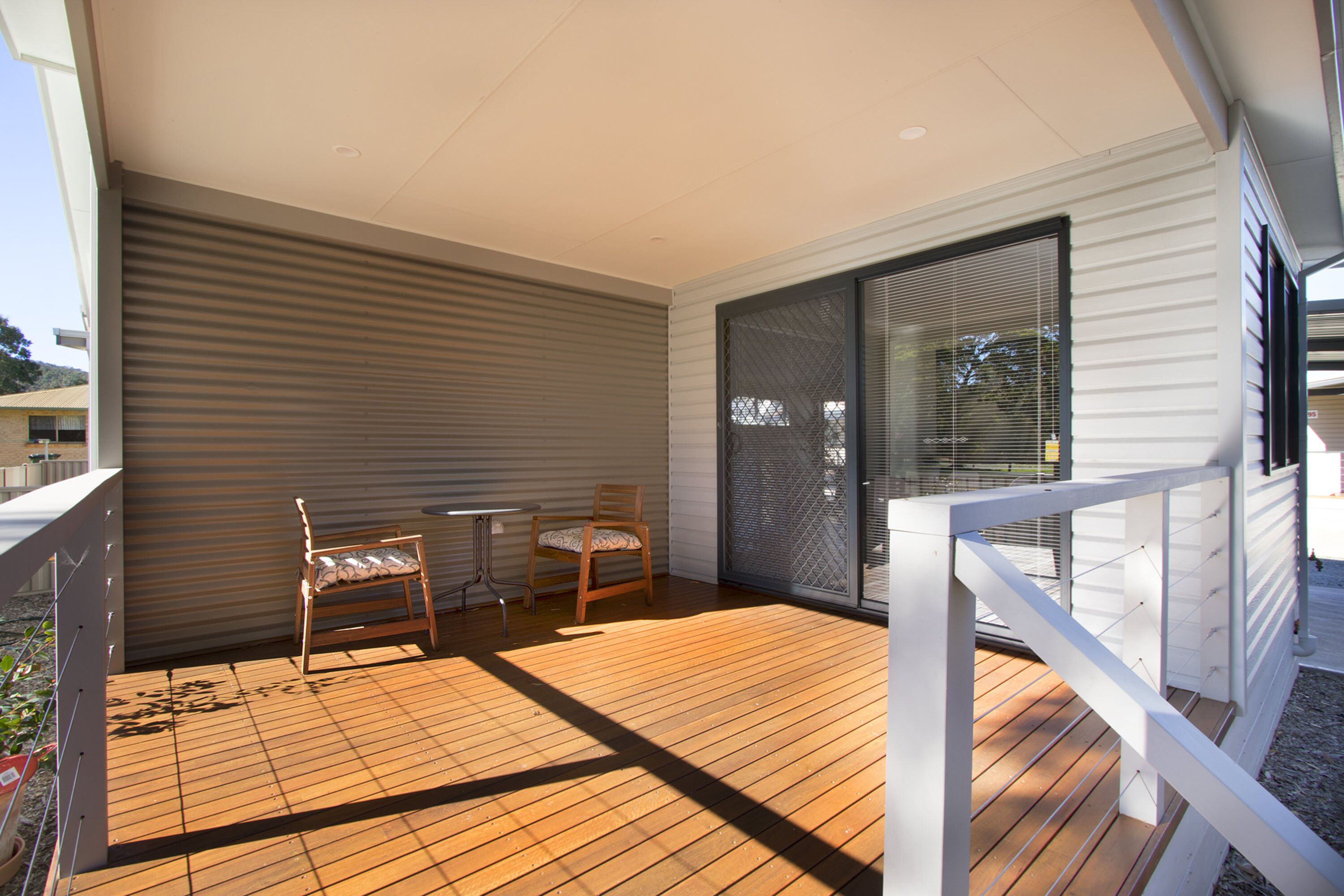 A covered outdoor area with a wooden deck, two wooden chairs, and a table.