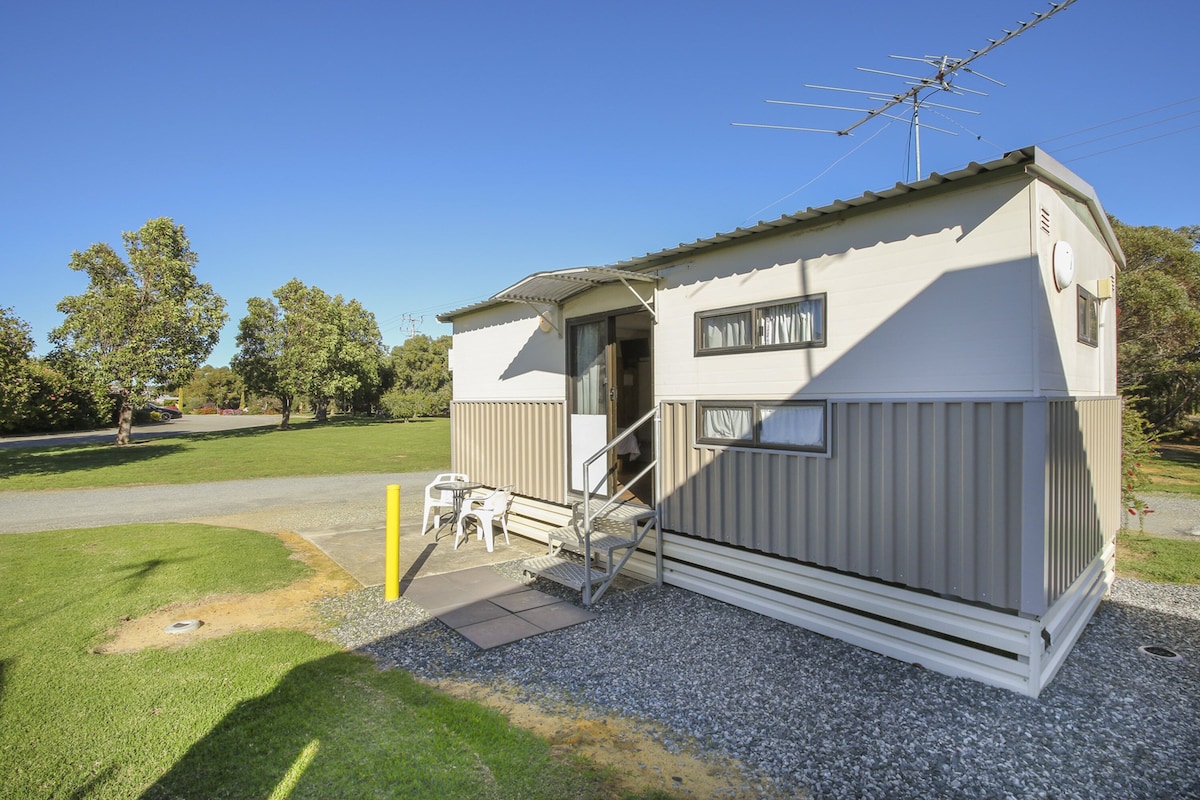 A small, single-story mobile home with a porch and a staircase leading to the entrance.