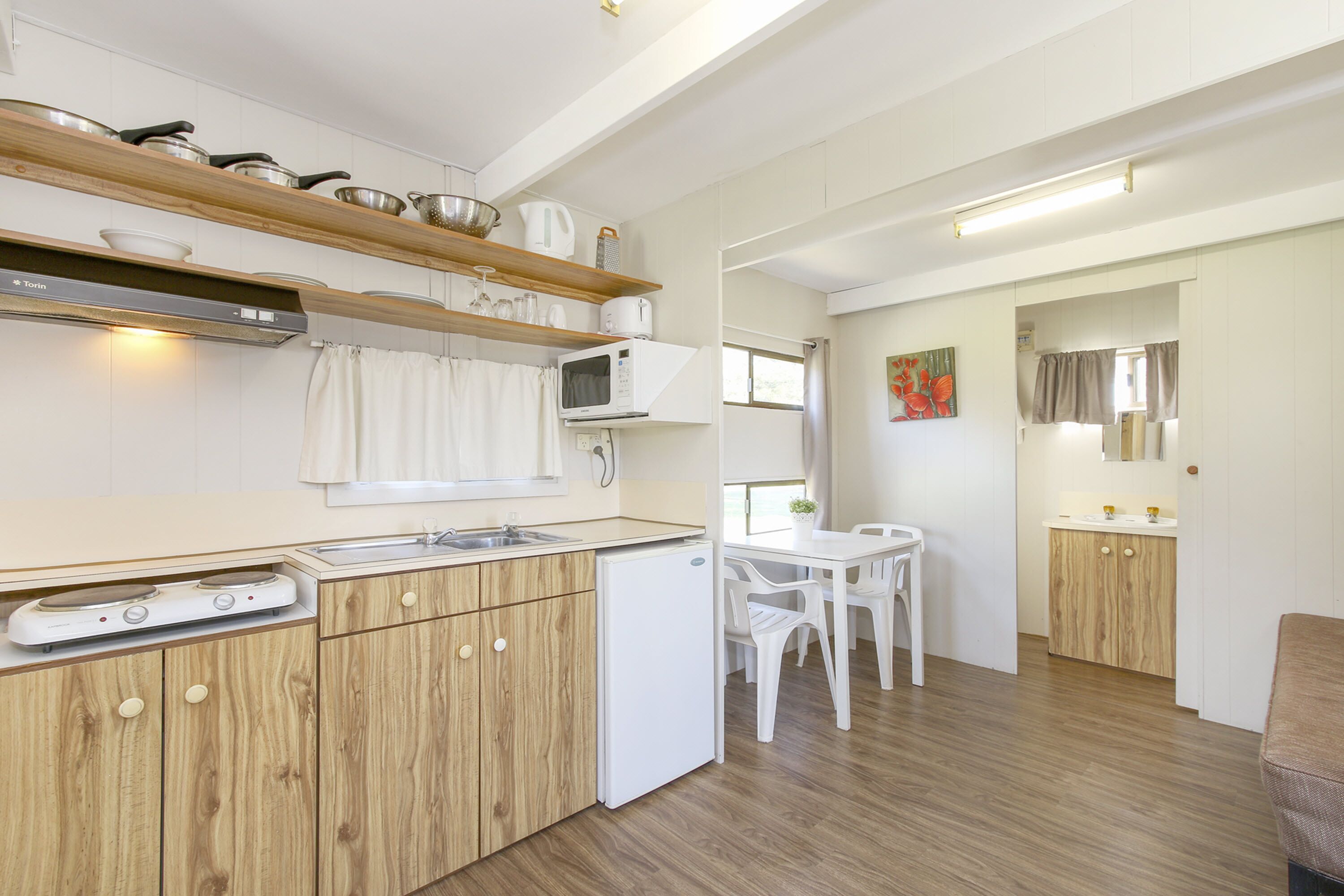 Une cuisine compacte avec des meubles en bois, un four à micro-ondes et un petit réfrigérateur. On y trouve également un coin repas avec une table et des chaises blanches.
