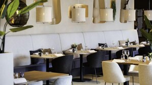 Ein modernes Restaurant mit runden Tischen und Stühlen, einer weißen, gepolsterten Sitzbank und wandmontierten Pendelleuchten.